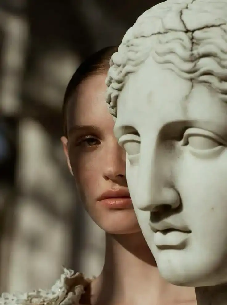Rostro de una mujer junto a un busto de mármol.