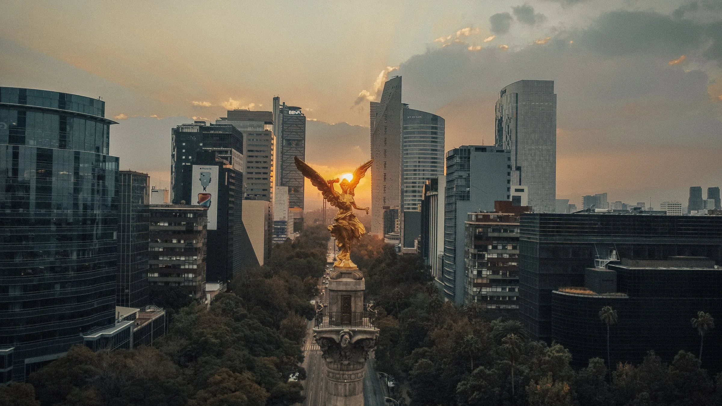 El Ángel de la Independencia frente al sol del atardecer y los edificios de Paseo de la Reforma.